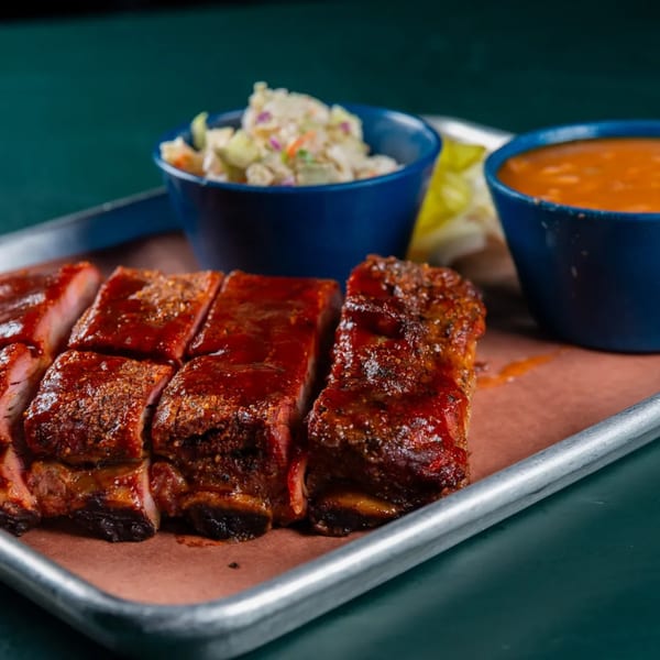 Ace's BBQ ribs with coleslaw and baked beans on a metal tray.