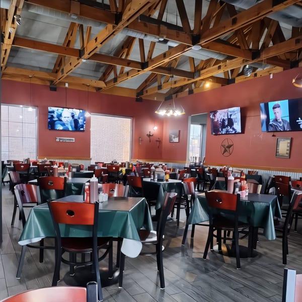 Interior of Ace's BBQ with red walls, exposed wooden beams, and tables set with red and green tablecloths.