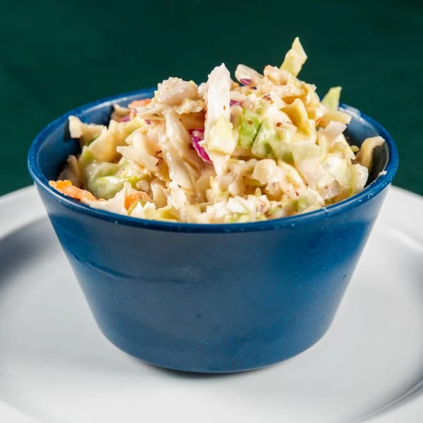 Creamy coleslaw with shredded cabbage, carrots, and red onion in a blue bowl.