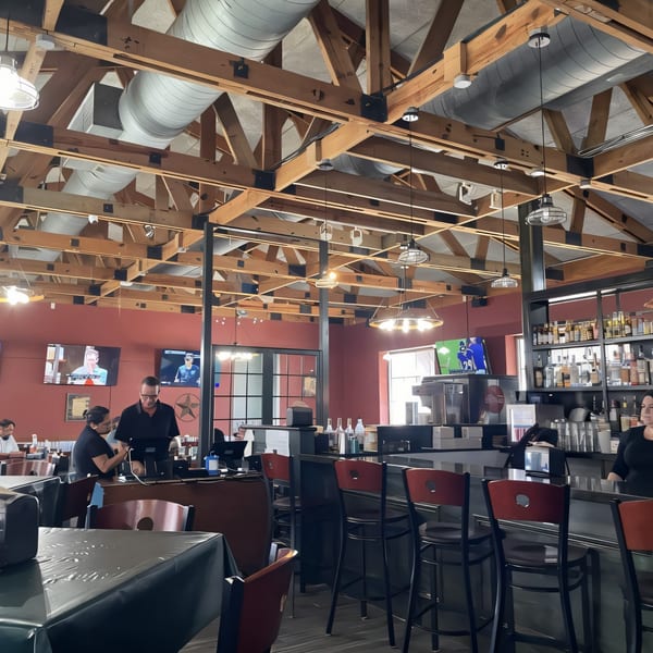 Interior of Ace's BBQ with exposed wooden beams, red walls, a bar, and staff working.