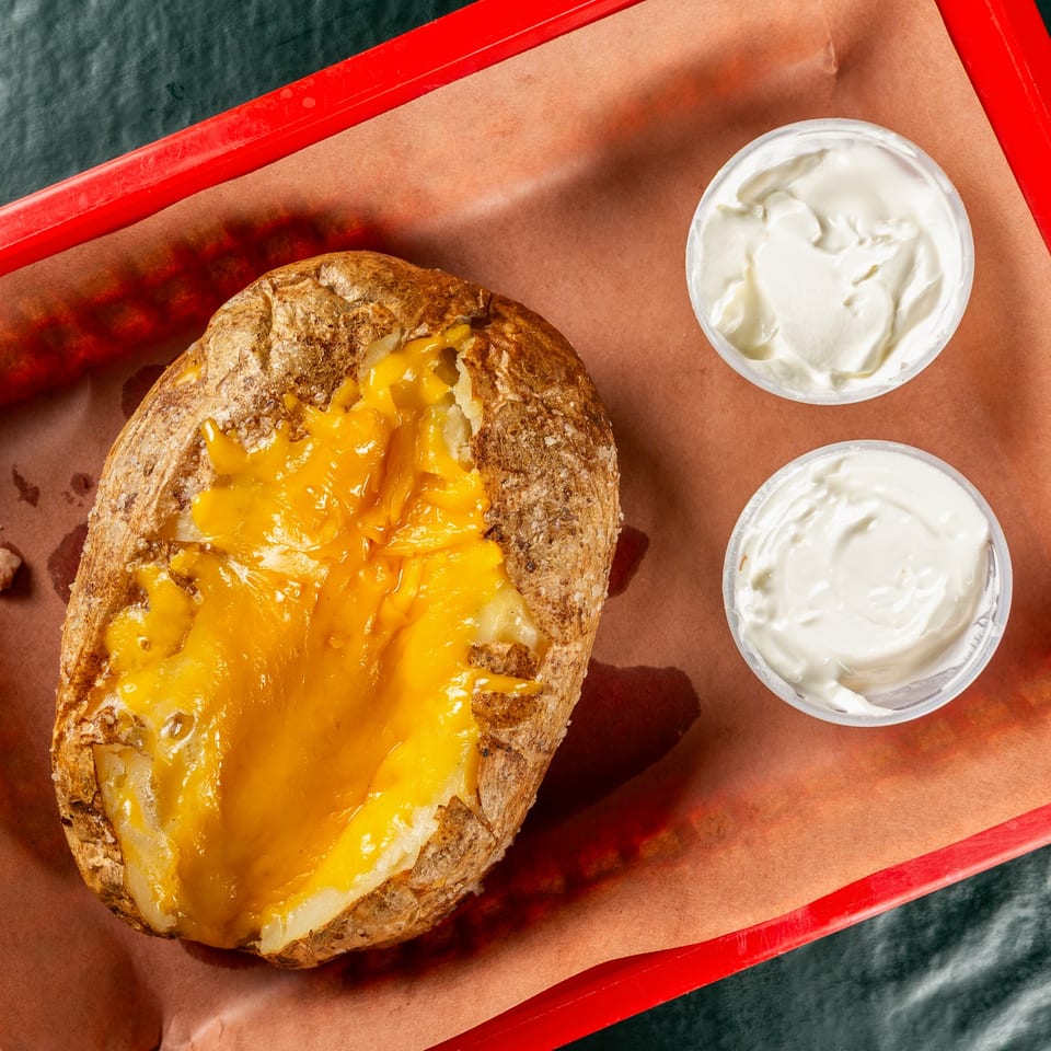 Baked potato topped with melted cheese and two containers of sour cream on a red tray.