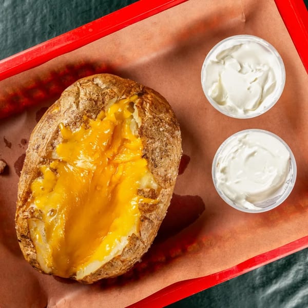 A baked potato topped with melted cheddar cheese, served with two cups of sour cream.