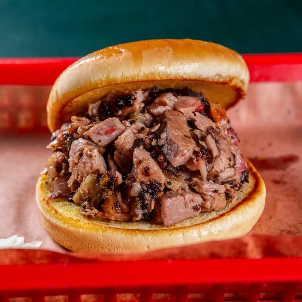 Close-up of a juicy Ace's BBQ chopped brisket sandwich on a toasted bun in a red basket.