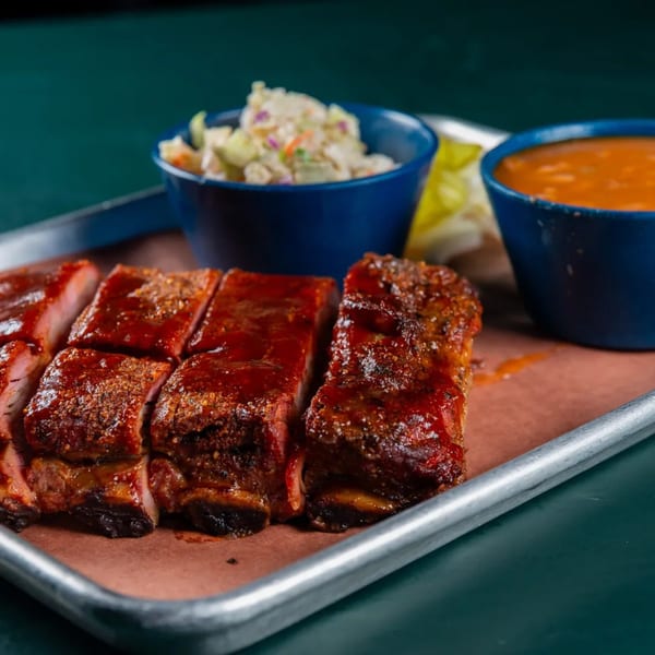 Ace's BBQ ribs with coleslaw and baked beans in blue bowls on a metal tray.