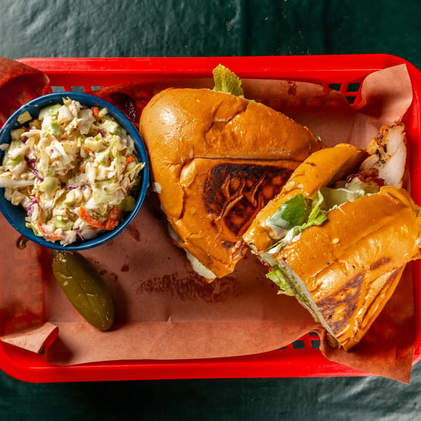 Ace's BBQ chicken sandwich with coleslaw and a pickle in a red basket.
