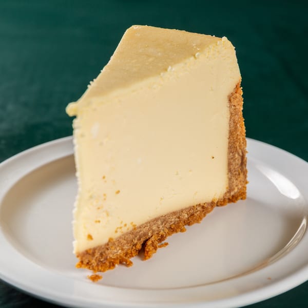 A slice of creamy cheesecake with a thick graham cracker crust on a white plate.
