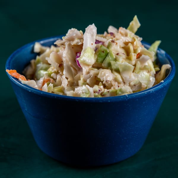 Creamy coleslaw with shredded cabbage, carrots, and red onion in a blue bowl.