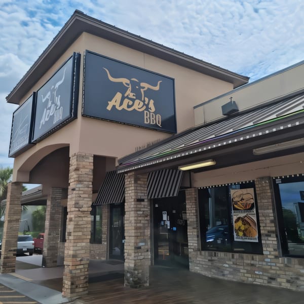 Exterior of Ace's BBQ restaurant with large signs featuring a bull logo and striped awnings.