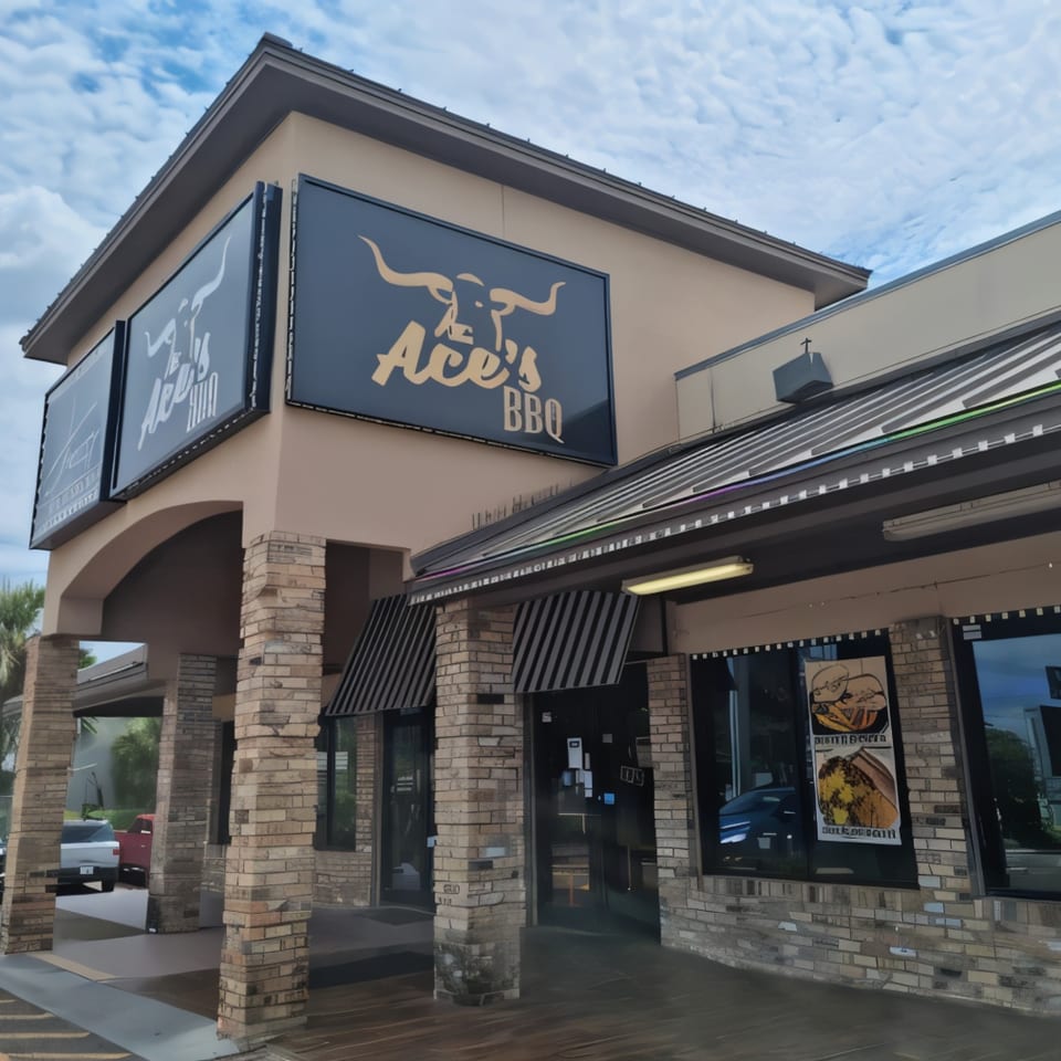 Exterior of Ace's BBQ restaurant with large signs featuring a bull logo and striped awnings.
